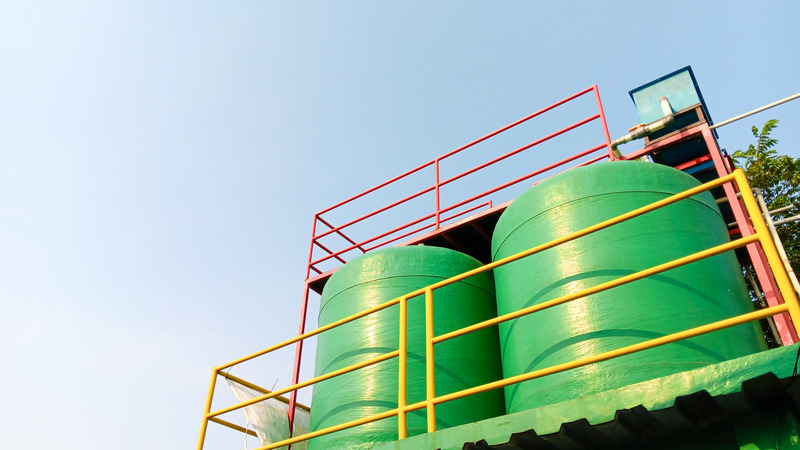 Two green garden water tanks installed outside beside plants encased in yellow and red painted steel